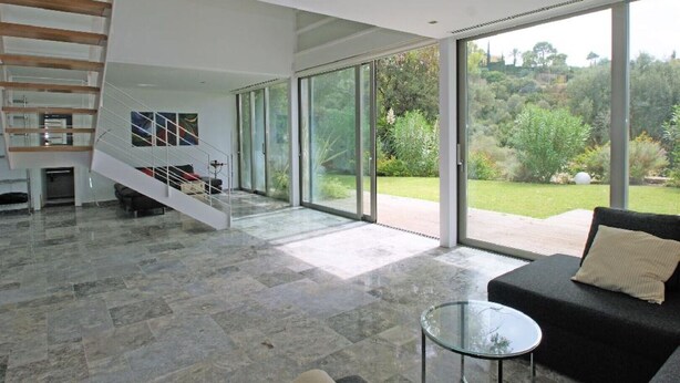 A spacious living area with a modern staircase, large glass doors leading to a garden, and a glass coffee table. - Villa zu Vermieten in Porto del Almendros, Los Arqueros, Benahavis (Benahavís)