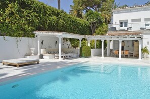A pool area with a covered seating area, a lounge chair, and a small table. - Villa im Spanischen Stil mit Moderner Dekoration (Marbella)