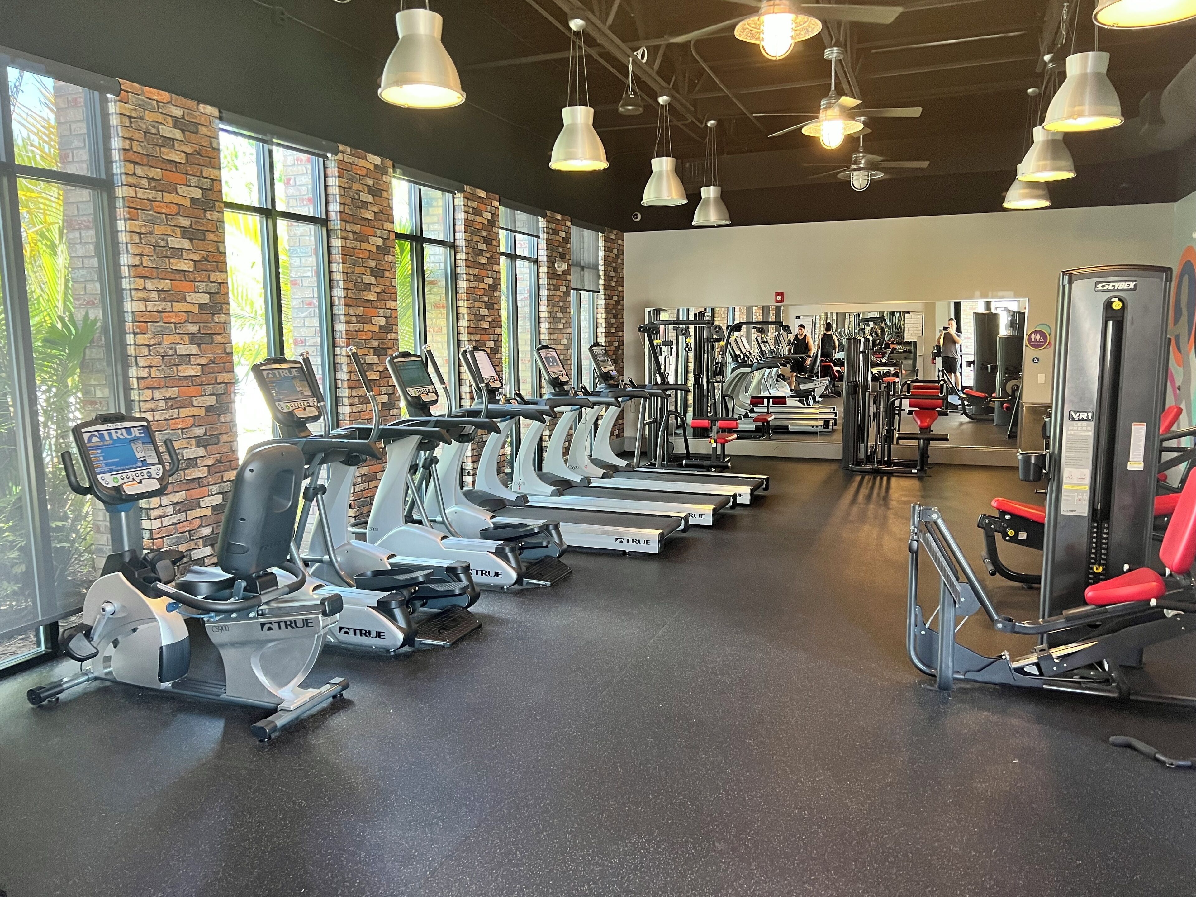 Ein Fitnessstudio mit mehreren Laufbändern, Trainingsgeräten und einem großen Spiegel.