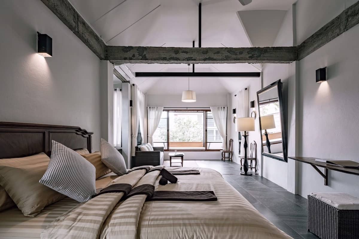 A bedroom with a large bed, a desk, a chair, and a window with curtains.