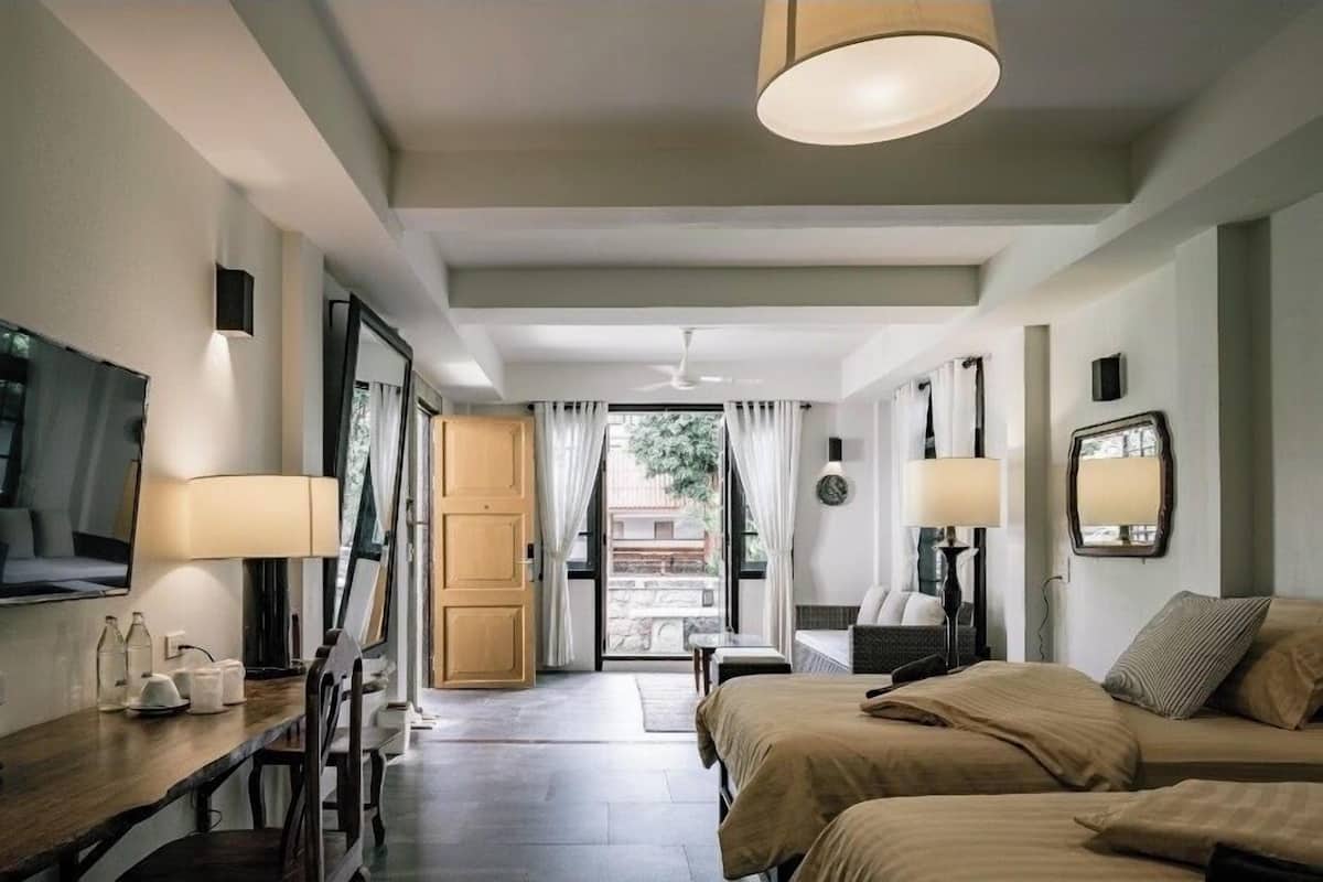 A hotel room with a bed, bedside tables, a desk, a chair, a TV, and a window with curtains.