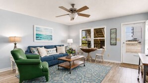 A living room with a blue sofa, a green armchair, a coffee table, a ceiling fan, and a view of the outside through a window. - By the Sea, on Perdido Key Dr! (Pensacola)