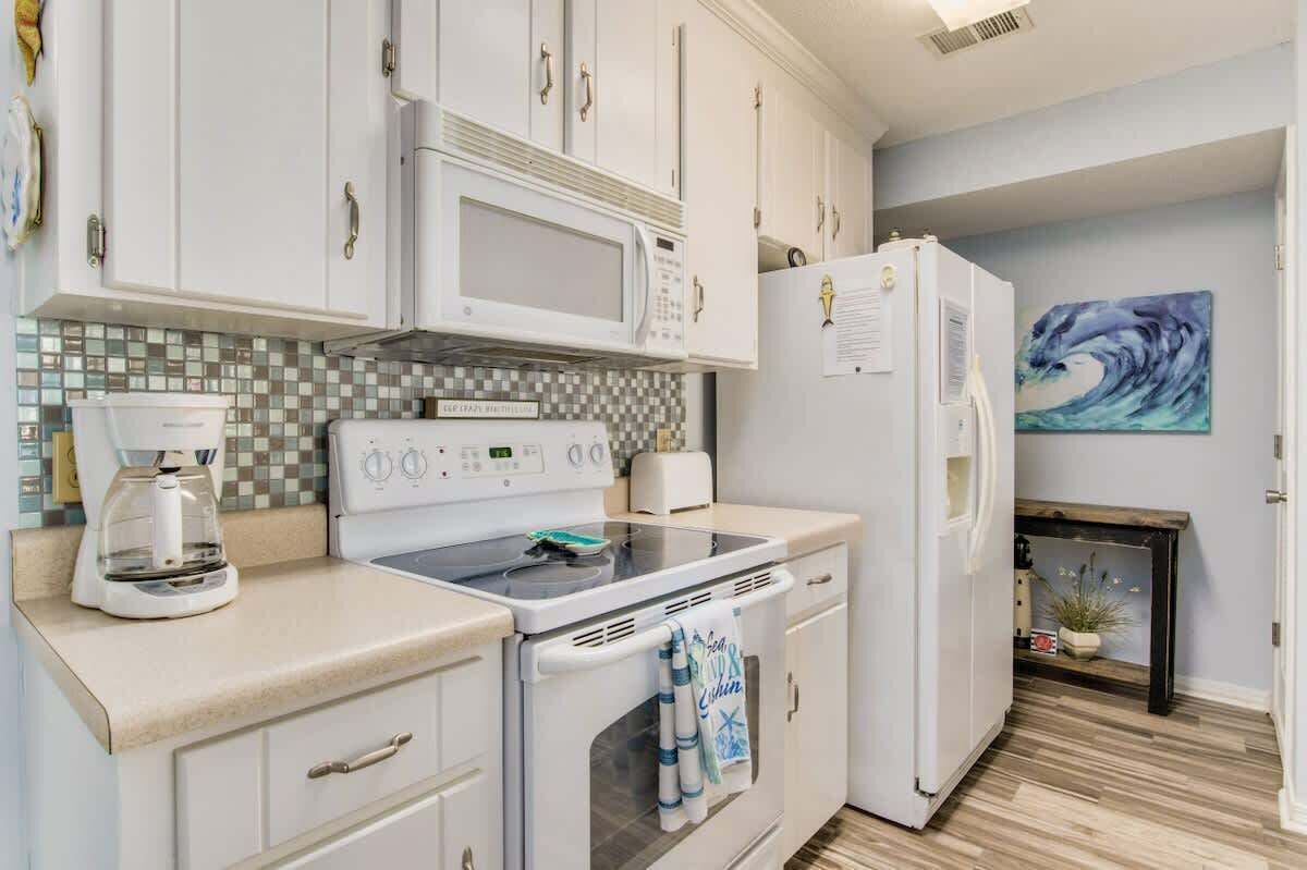 Una cocina moderna con armarios blancos, un microondas, una estufa y un refrigerador.