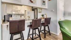A modern kitchen with white cabinets, a central island with bar stools, and decorative wall art. - By the Sea, on Perdido Key Dr! (Pensacola)