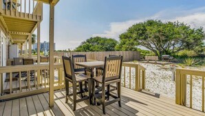 A wooden deck with a table and chairs, overlooking a sandy area with trees and a wooden fence. - By the Sea, on Perdido Key Dr! (Pensacola)