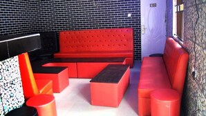 A red sofa set against a black and white tiled wall, with a small table and a red cylindrical stool in the foreground. - Laurel Blue Suites (Port Harcourt)