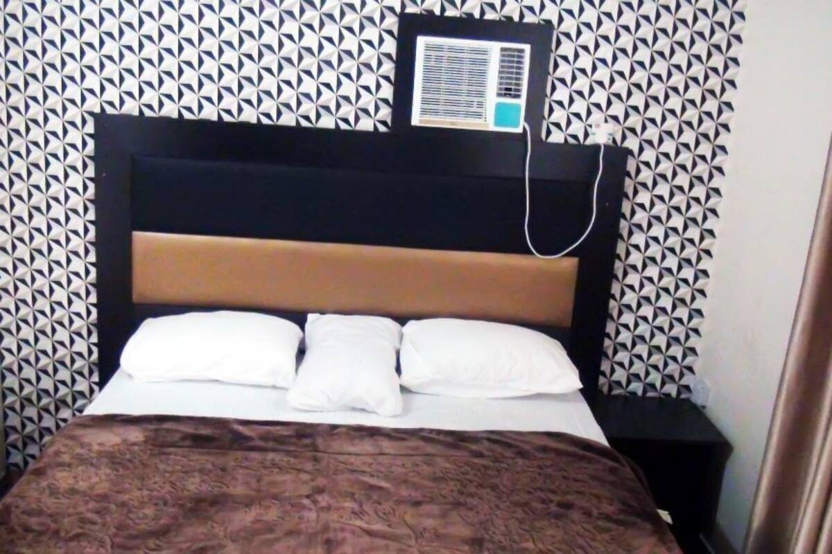 A bed with a patterned headboard, a bedside table, and a wall-mounted air conditioner.
