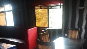 A dining area with a table and chairs, a red sofa, and a window with blinds. - Laurel Blue Suites (Port Harcourt)