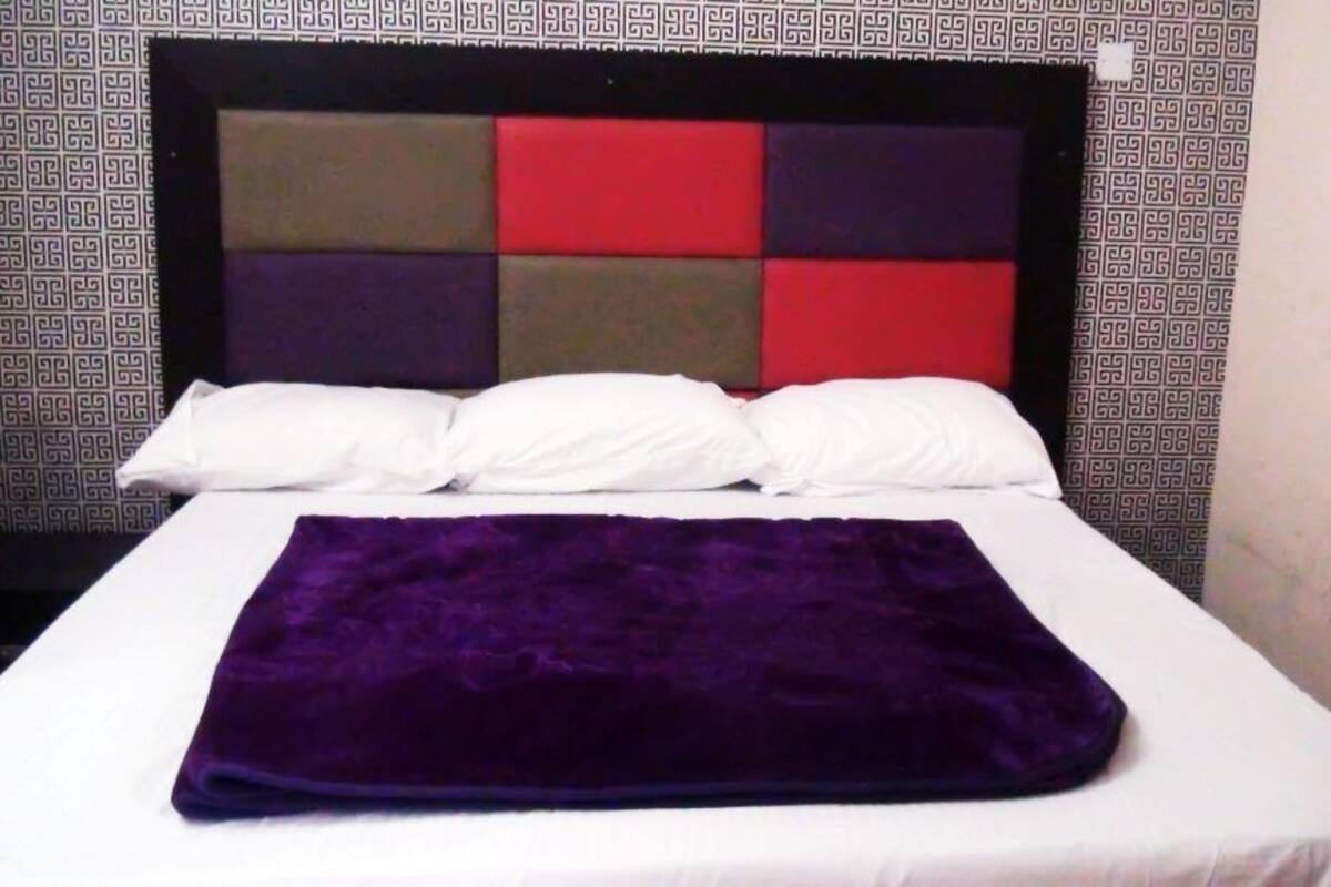 A bed with a white mattress and a purple blanket, a headboard with a geometric pattern, and a patterned wall.