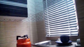 A kitchen with a sink, a window with blinds, and a gas cylinder. - Laurel Blue Suites (Port Harcourt)