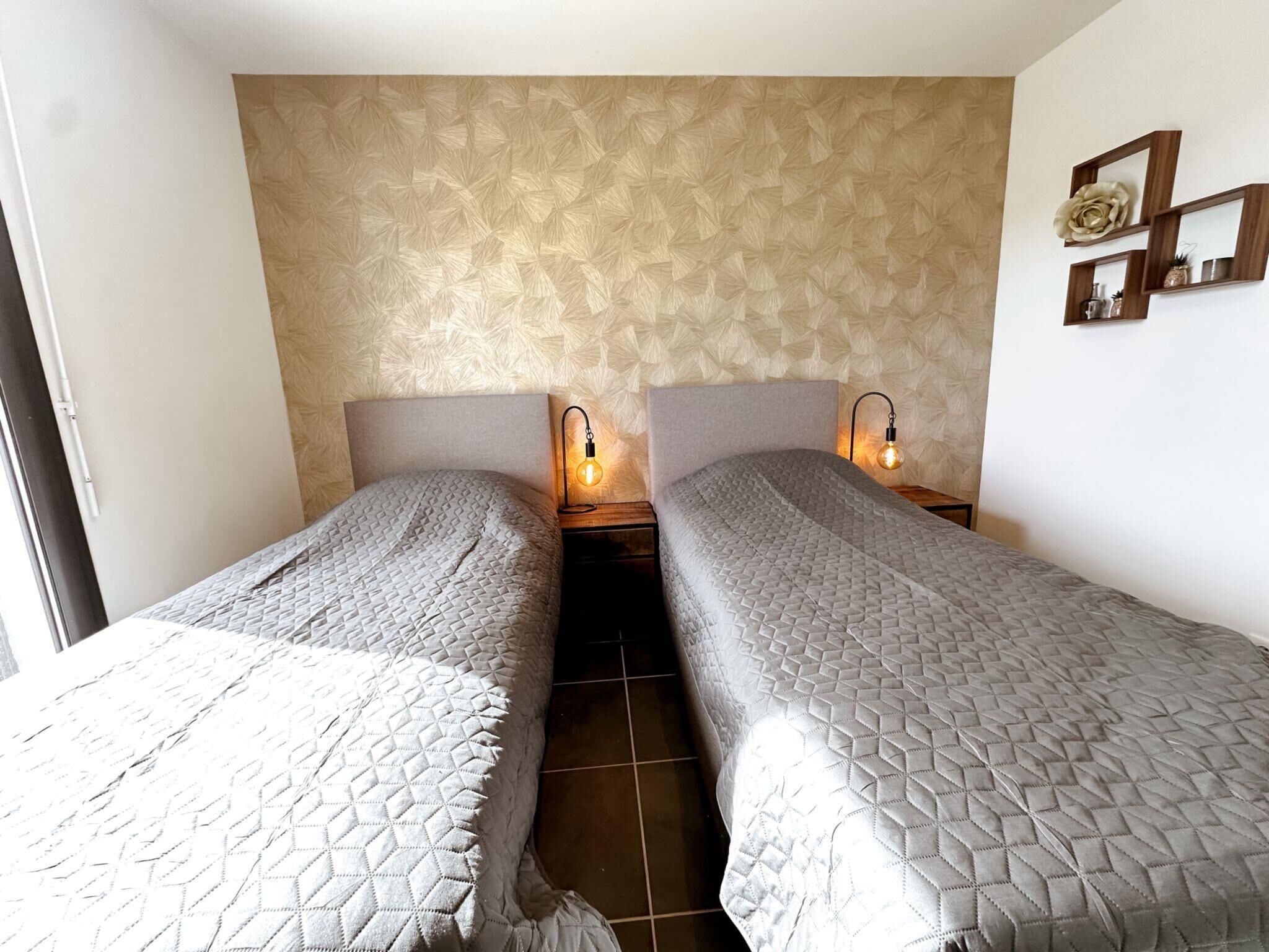 Een kamer met twee eenpersoonsbedden, elk met hoofdbord, nachtkastje en een wandlamp.