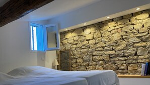 A bedroom with a stone wall, a bed, a window, and a wooden beam ceiling. - Great house with beautiful (sundowner) view (Saint-André-d’Olérargues)