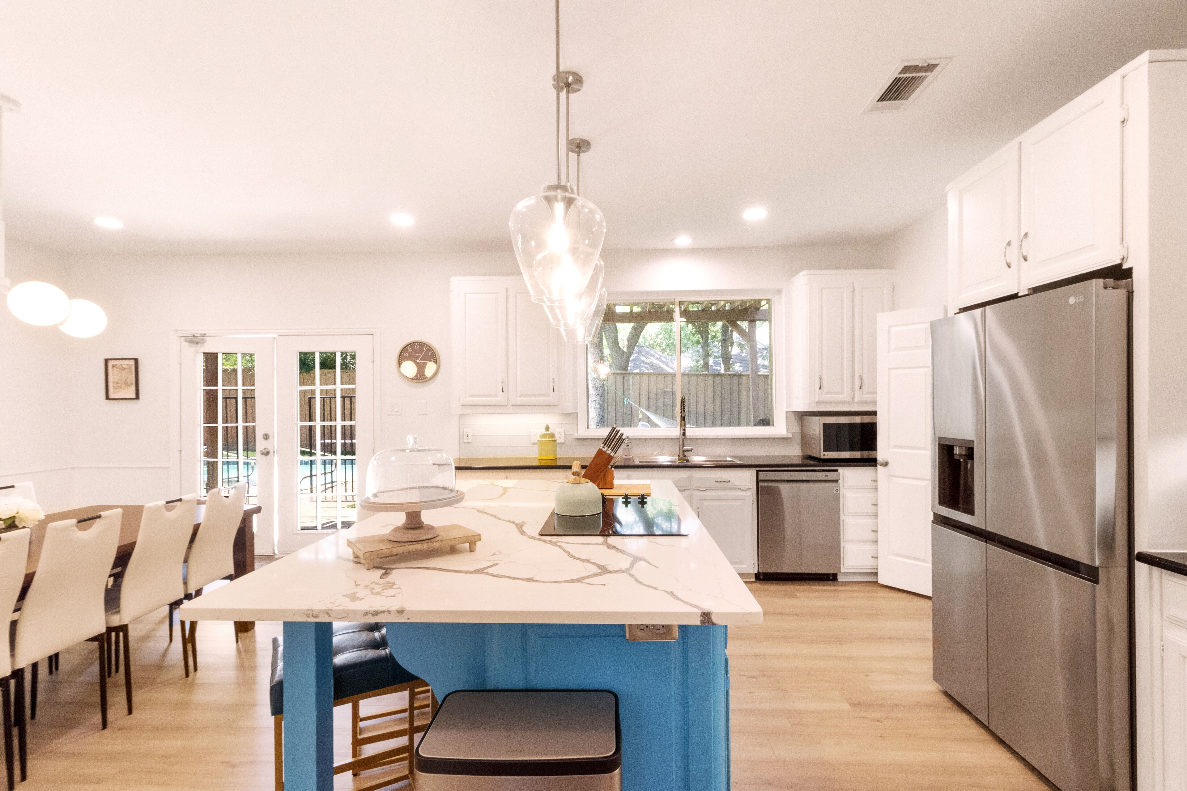 A modern kitchen with white cabinets, a stainless steel refrigerator, and a marble island.