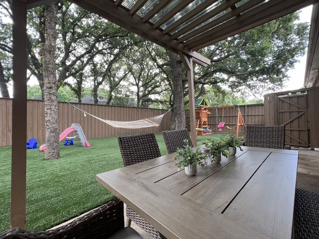 An outdoor patio with a wooden table and chairs, surrounded by a wooden fence and trees.