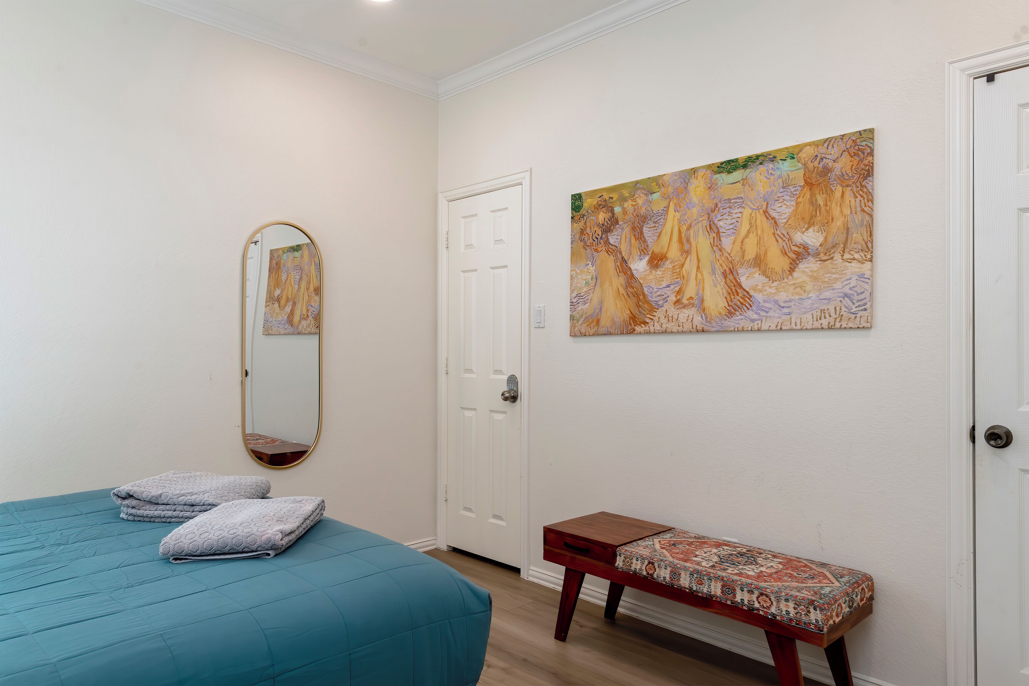 A bedroom with a bed, a bench, a painting, and a door.