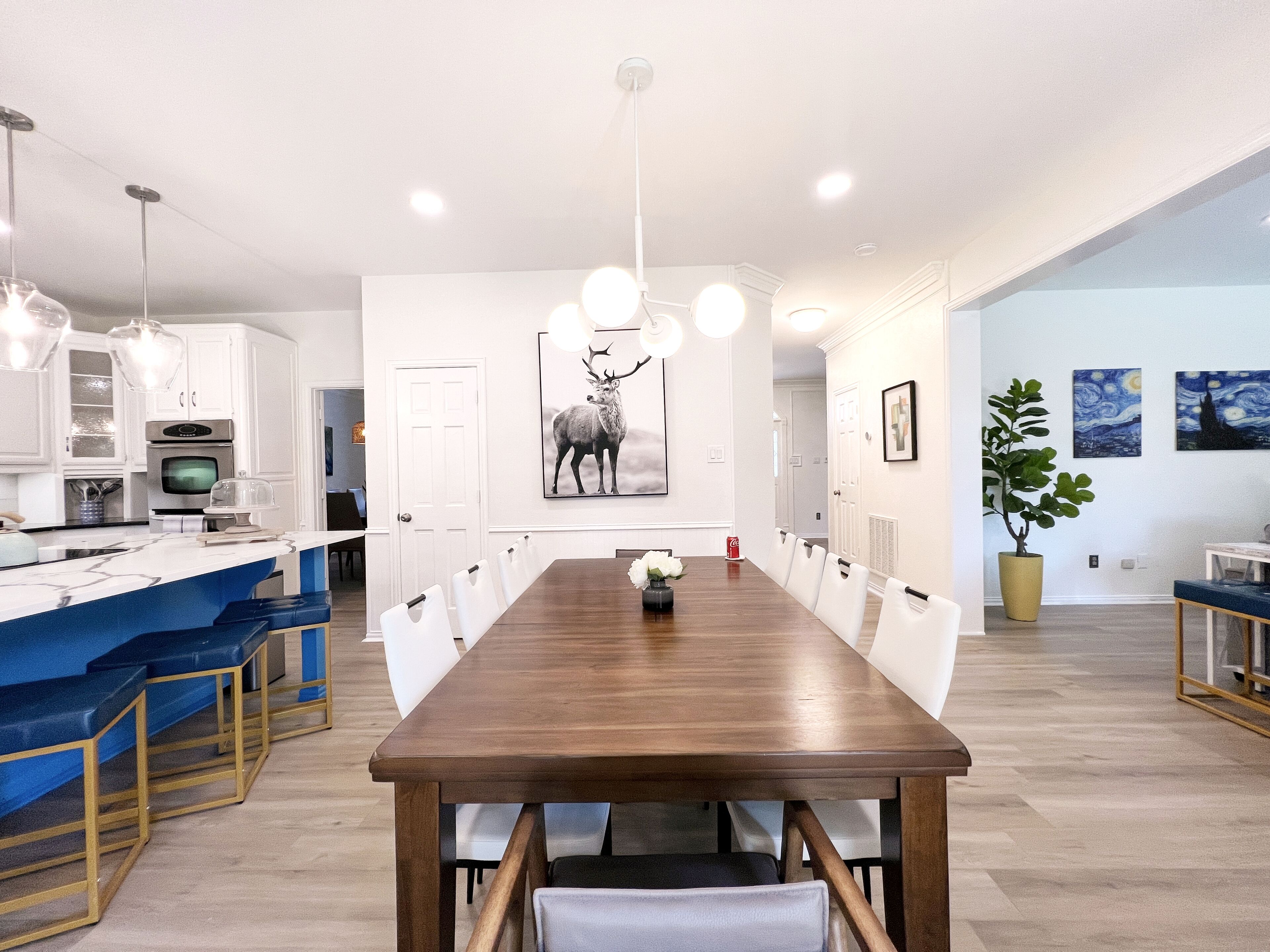 Een moderne keuken met witte kasten, een ingebouwde oven en een eethoek met een lange houten tafel en witte stoelen.