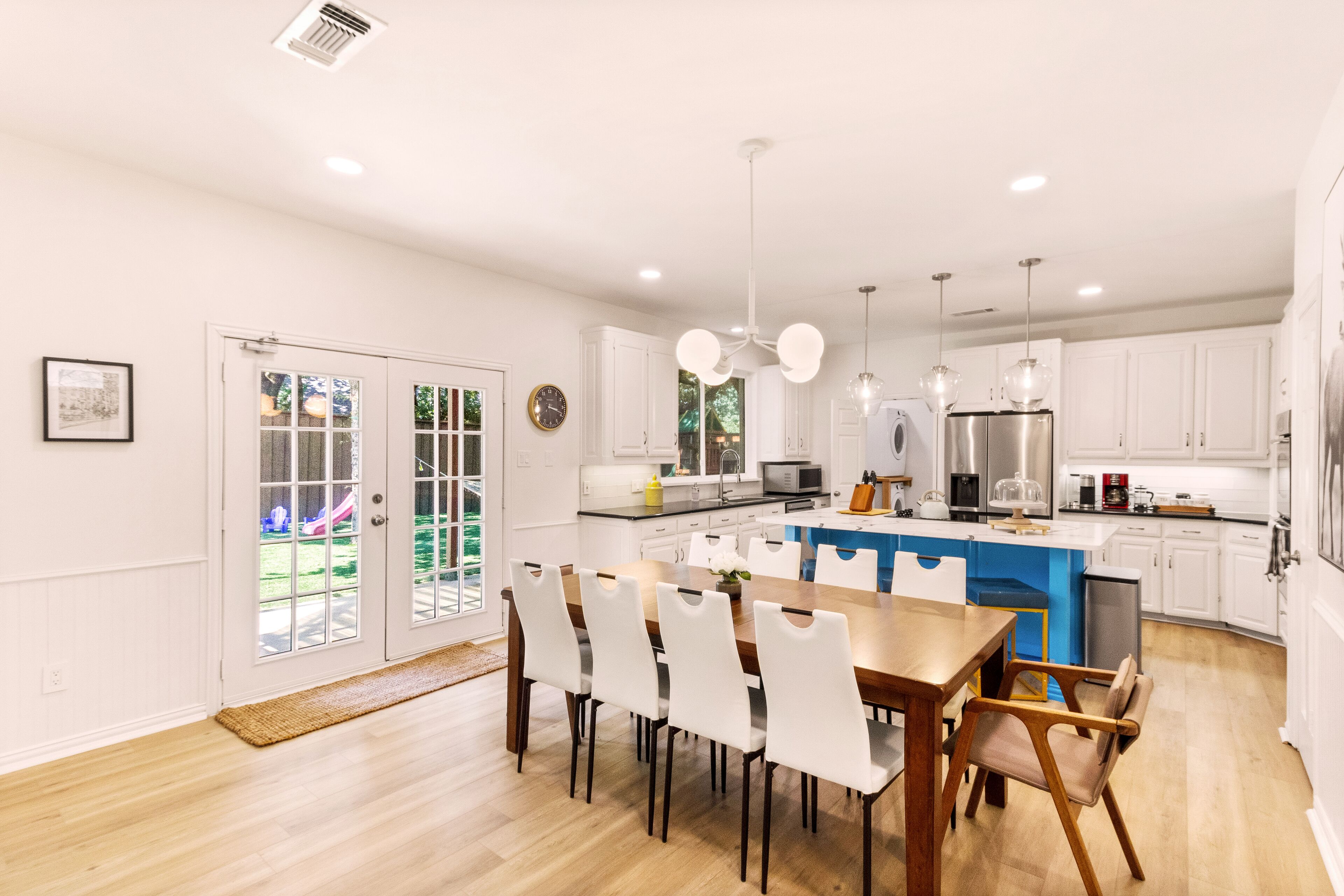 A modern kitchen with white cabinetry, a central island, and a dining area with white chairs.