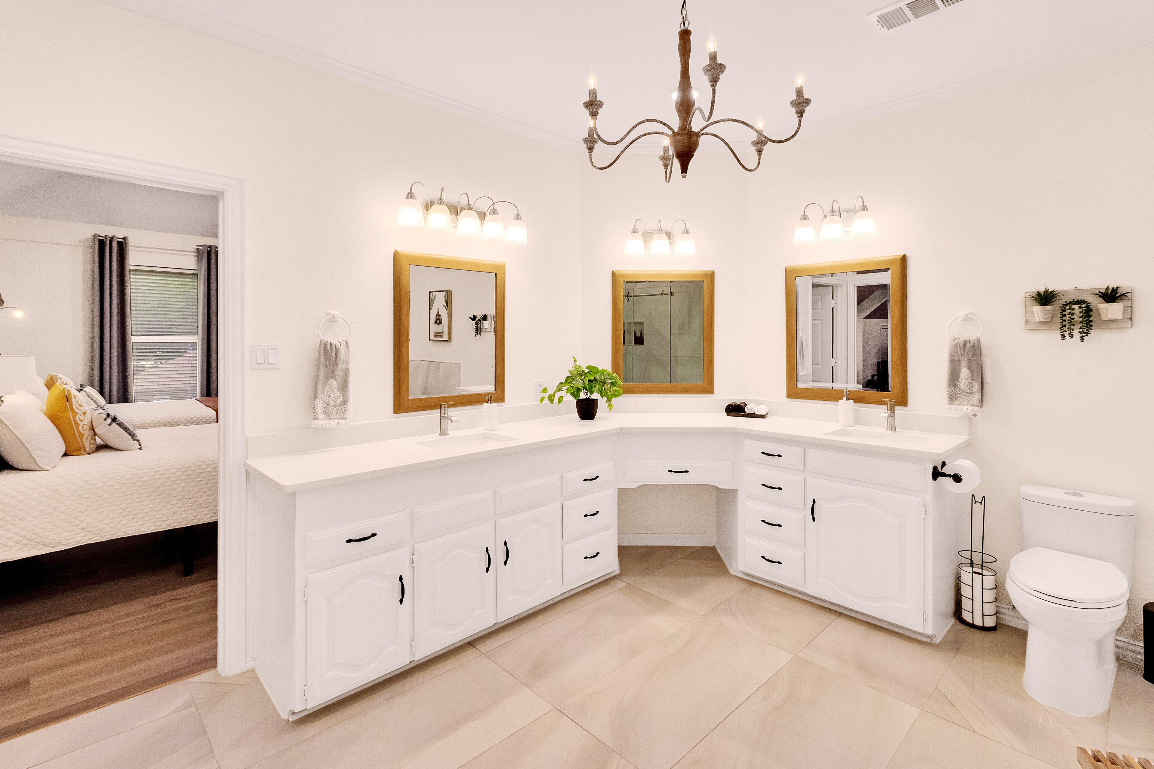 A modern bathroom with white cabinetry, a large mirror, and a chandelier.
