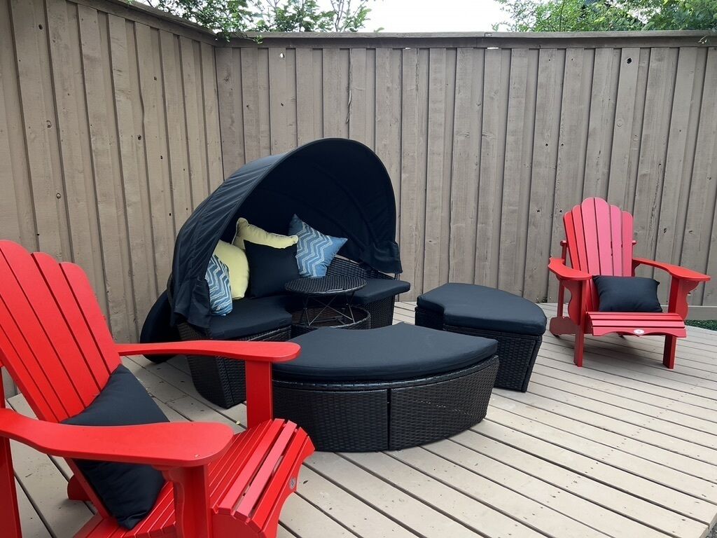 Una terraza con una zona de estar circular al aire libre, dos sillas Adirondack rojas y un área de estar cubierta con cojines.
