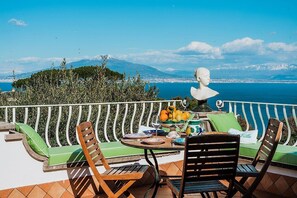 Una terraza con una mesa lista para comer, una escultura de busto y vistas al mar y a las montañas.