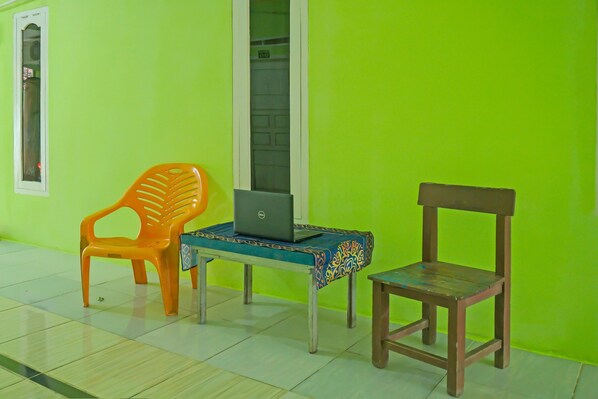 A room with a green wall, a wooden chair, an orange plastic chair, and a table with a laptop.