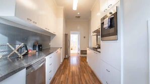 A narrow kitchen with white cabinets, a wooden floor, and a stainless steel range hood. - Cambridge House, Bendigo (Bendigo)