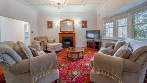 A living room with two sofas, a coffee table, a fireplace, a television, and a large window. - Cambridge House, Bendigo (Bendigo)