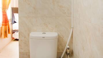 A bathroom with a white toilet, marble walls, and a shower area.