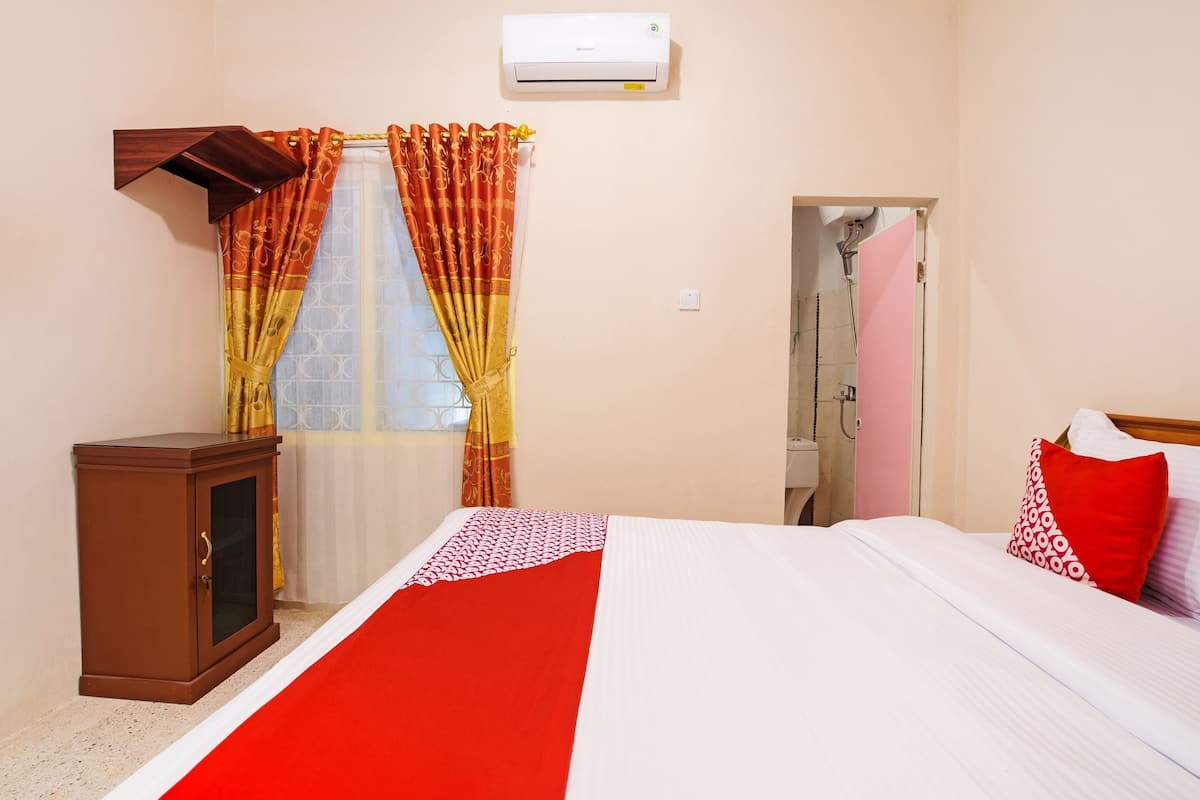 A hotel room with a bed, a wardrobe, a shower, and an air conditioning unit.