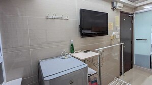 Ein kleines, modernes Badezimmer mit grauen Fliesen, einem angebrachten Flachbildfernseher, einem kleinen Waschbecken mit Spiegel und einem Handtuchhalter.