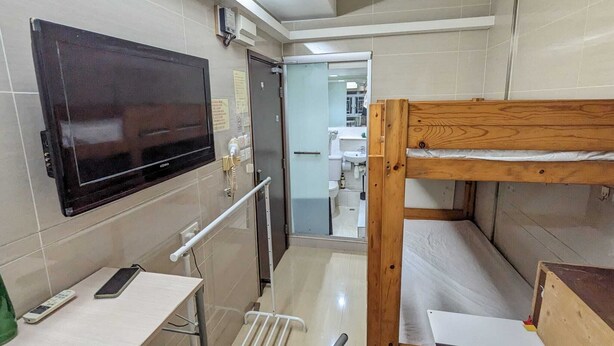 Ein schmales Badezimmer mit einem hölzernen Etagenbett, einem an der Wand befestigten Fernseher und einem kleinen Tisch mit Telefon und Flasche.