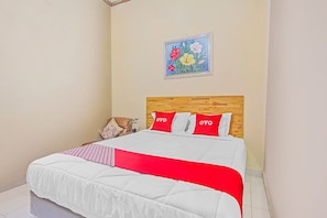 A neatly made bed with a wooden headboard, a red and white bedspread, and two pillows with 'OYO' branding.