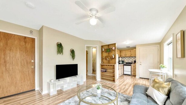 A modern living room with a flat-screen TV, a marble coffee table, a grey sofa, wooden flooring, and a ceiling fan.