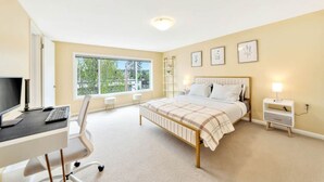 A bedroom with a bed, desk, chair, and a large window.