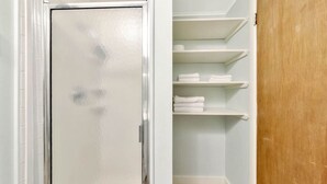 A bathroom with a white door, a shower, and a storage area with shelves.