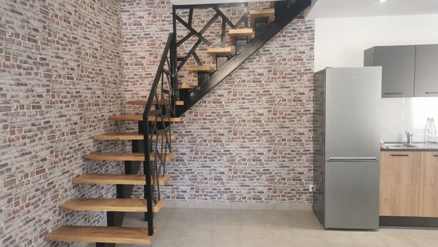 Una cocina moderna con pared de ladrillo, escalera de madera y refrigerador de acero inoxidable.
