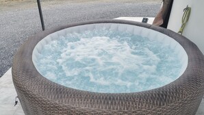 Un jacuzzi grande al aire libre con diseño de mimbre, rodeado por un área de grava y un piso de concreto.