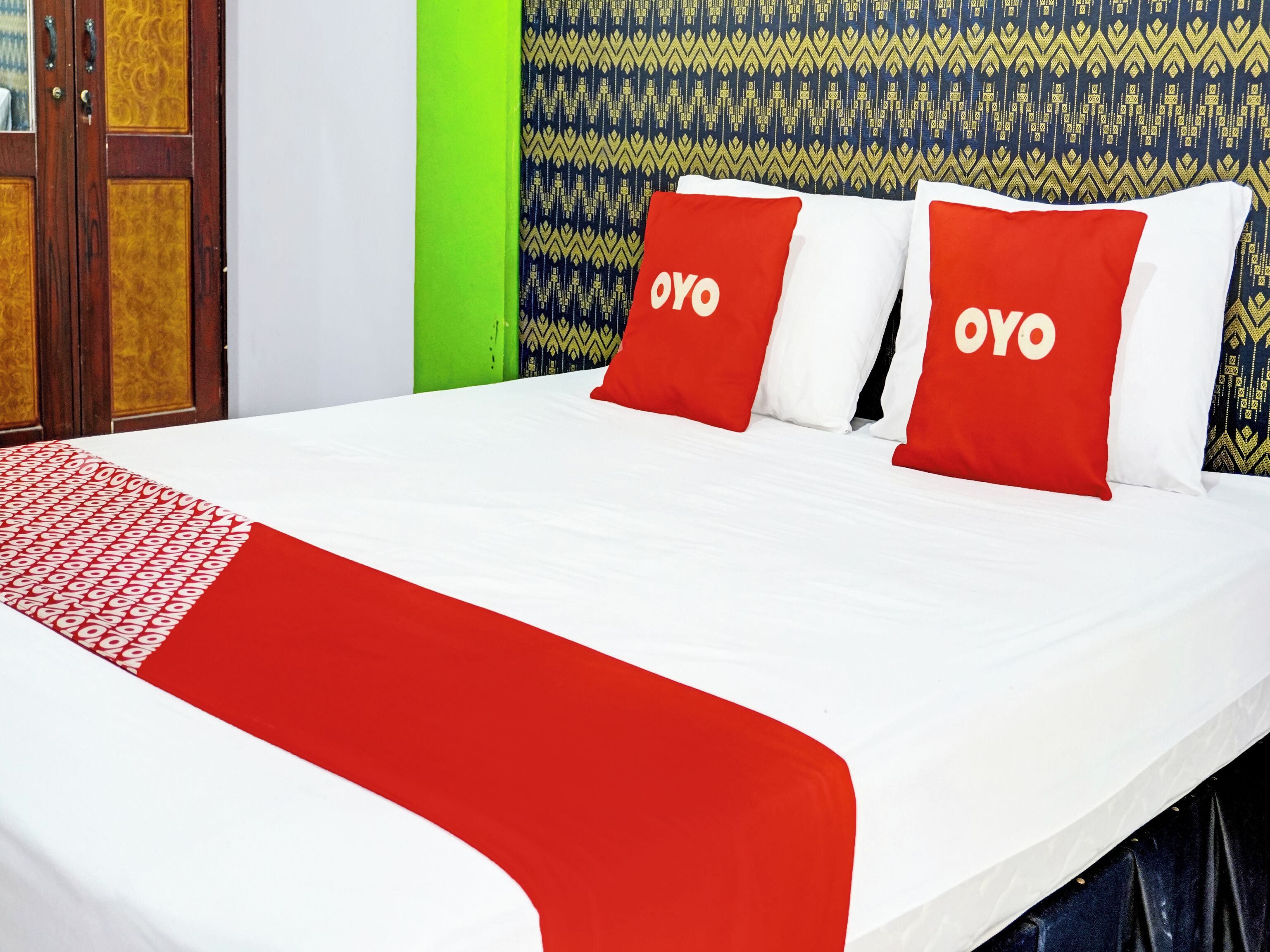 Ein Bett mit roter und weißer Bettwäsche, zwei Kissen mit 'OYO'-Branding, einer gemusterten Wand und einer grünen Akzentwand.