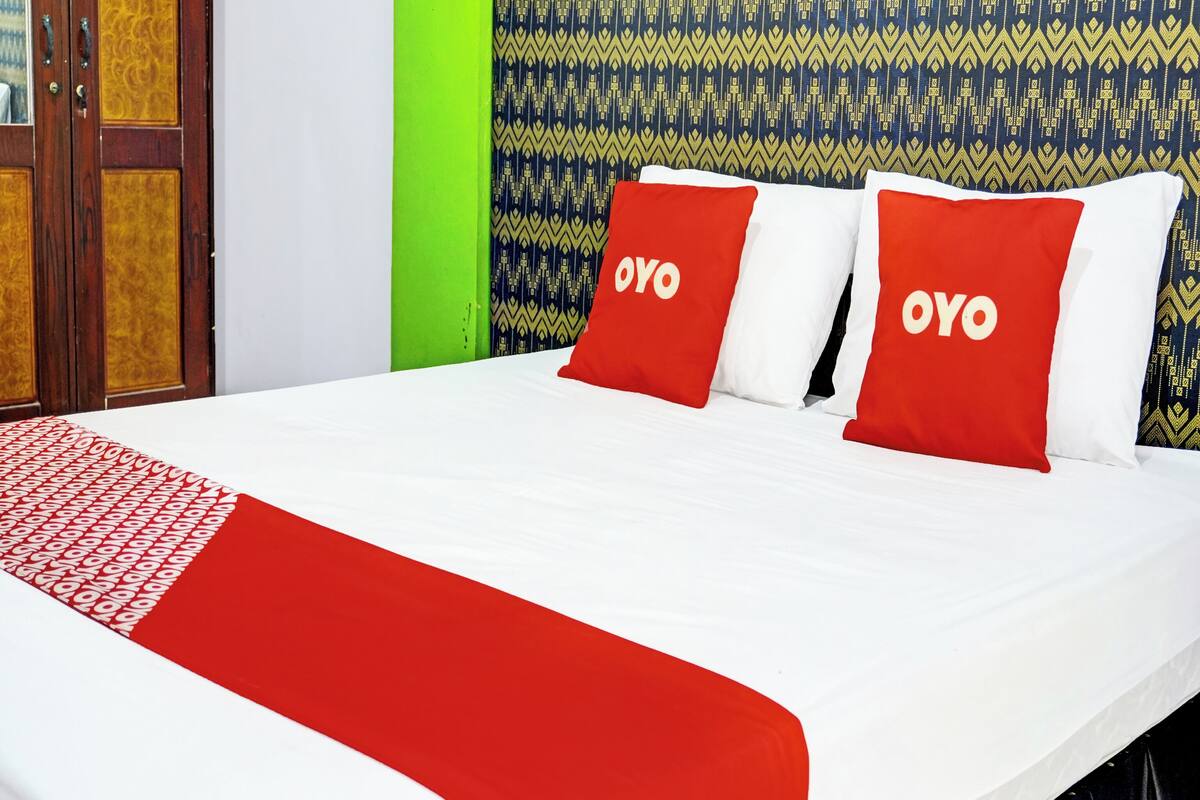 A bed with red and white bedding, two pillows with 'OYO' branding, a patterned wall, and a green accent wall.