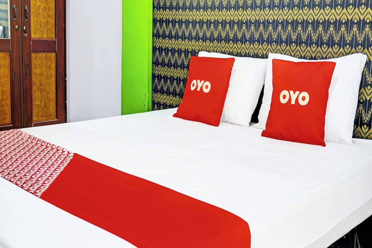 Ein Bett mit roter und weißer Bettwäsche, zwei Kissen mit 'OYO'-Branding, einer gemusterten Wand und einer grünen Akzentwand.