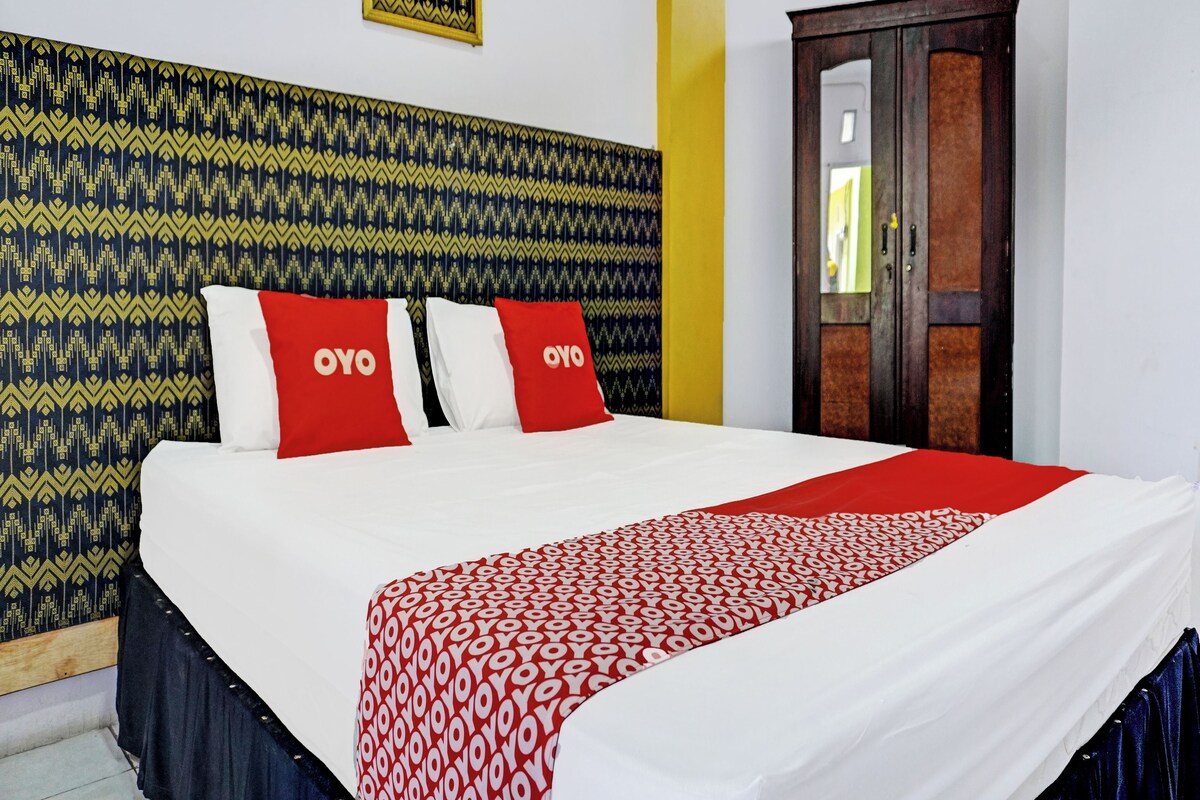 Ein Hotelzimmer mit einem gemusterten Kopfteil, einem Bett mit rot-weißer Bettwäsche und einer Holztür.