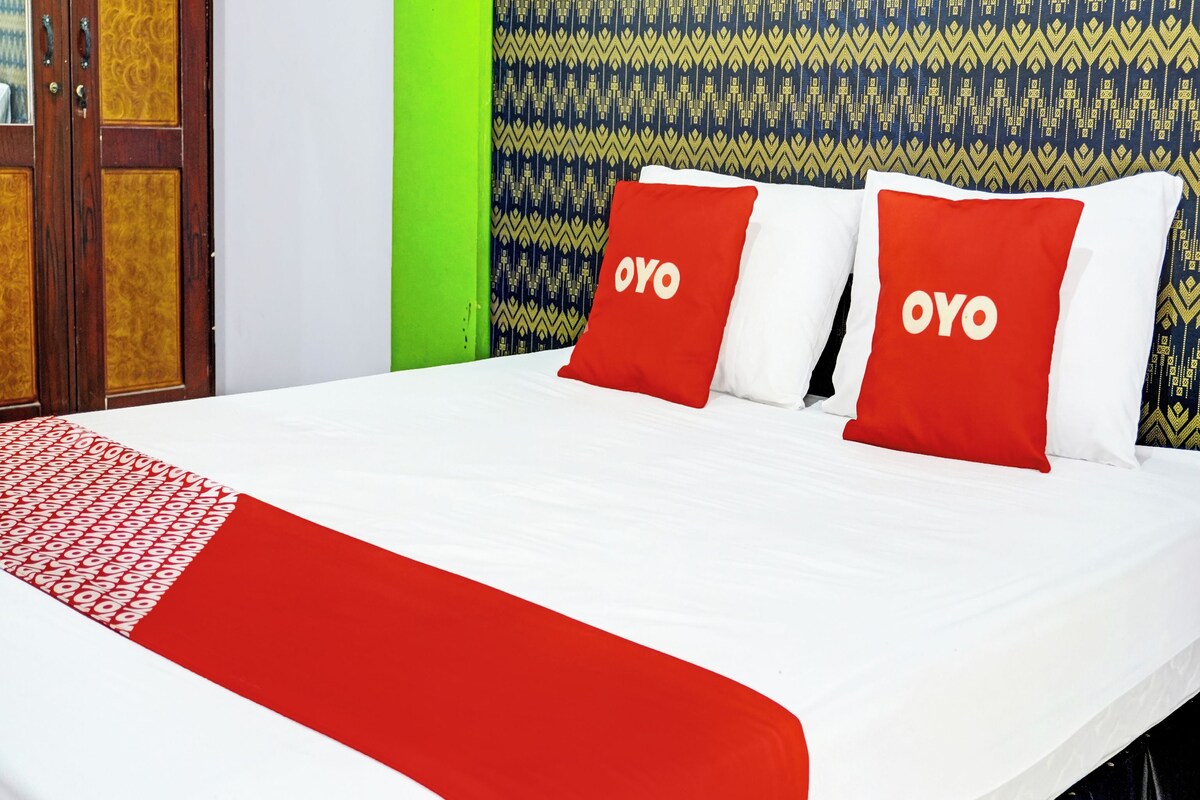 A bed with red and white bedding, two pillows with 'OYO' branding, a patterned wall, and a green accent wall.