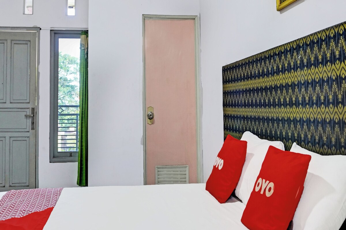 A hotel room with a bed, a door, a window, and a patterned wall.