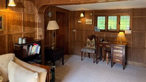 A room with wooden paneling, a desk with drawers, a chair, a bookshelf, and a lamp. - The Cottage Guest House (Bishop's Stortford)
