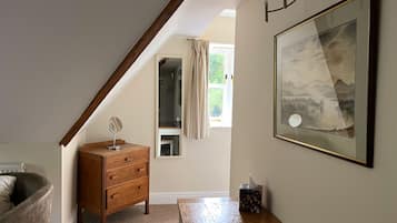 A bedroom with a wooden dresser, a bedside table, a framed picture on the wall, and a window with curtains.
