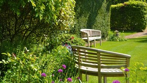 A garden with a wooden bench surrounded by lush greenery and purple flowers. - The Cottage Guest House (Bishop's Stortford)