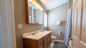 Un baño con tocador doble, inodoro, espejo iluminado y cortina de ducha.