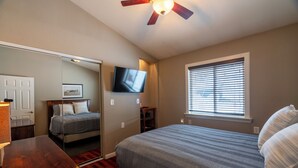 Un dormitorio con cama, ventilador de techo, televisor, ventana con persianas y puerta.