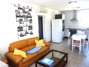A compact living space with a sofa, a glass coffee table, a kitchenette, and a dining area. - Los Olivos Residencial LEK (Peñiscola)