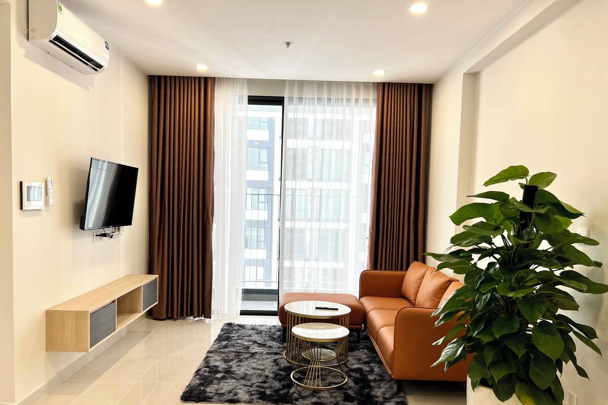 A modern living room with a sofa, a TV, a plant, and a large window with curtains.